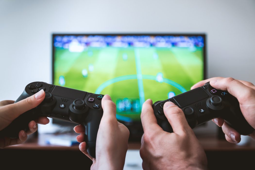 Two black ps5 controllers being held in front of a tv, a football game is playing.